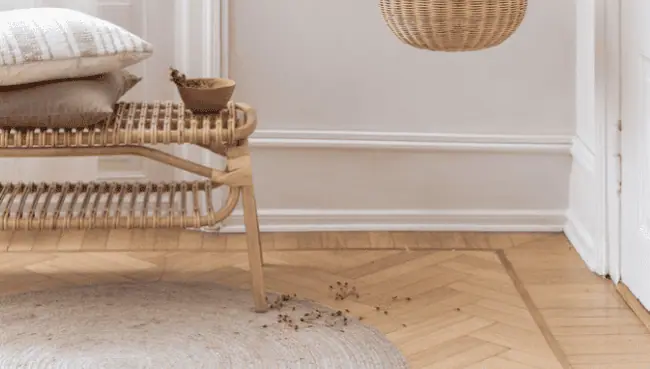 Kontainer DAM case thumbnail: Sika Design Sika Design wicker lamp hanging in a corner, close to a wicker bench, standing on a round nude-colored carpet atop fishbone flooring.