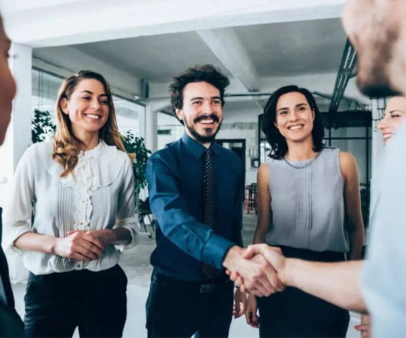 Become a parte Two people shaking hands with their colleagues around them