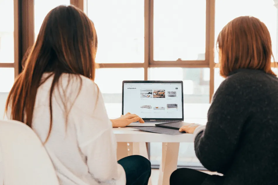 kobu-agency-7okkFhxrxNw-unsplash Two women sitting in front of a laptop, backs to the camera.