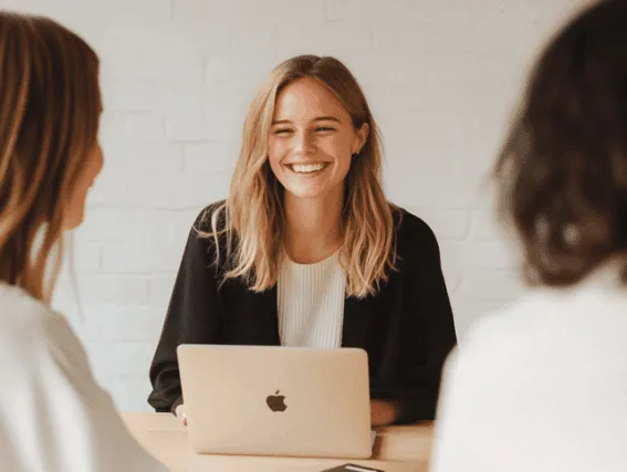 Smilende medarbejder i samtale med kolleger under møde, arbejder på bærbar computer — Kontainer Digital Asset Management (DAM) og Product Information Management (PIM) platform