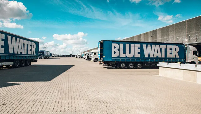 Blue Water trucks outside a warehouse under a blue sky.