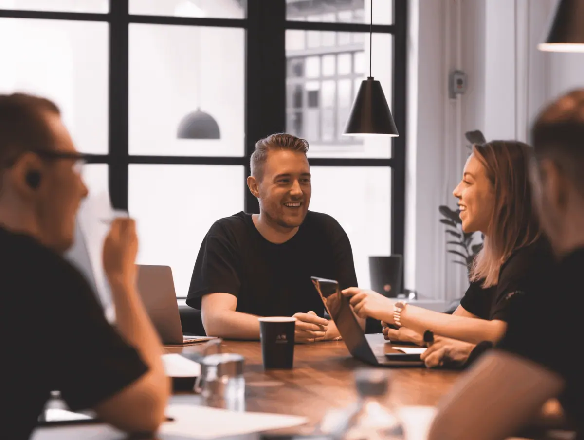 Teammøde med smilende kolleger, der samarbejder om digitale løsninger — Kontainer Digital Asset Management (DAM) og Product Information Management (PIM).