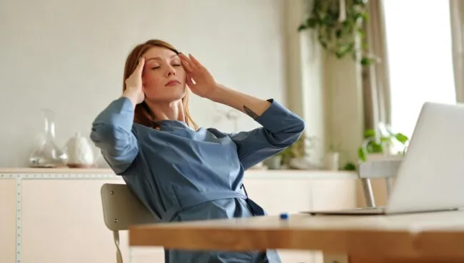 Stressed woman in office chair in front of pc leaning back