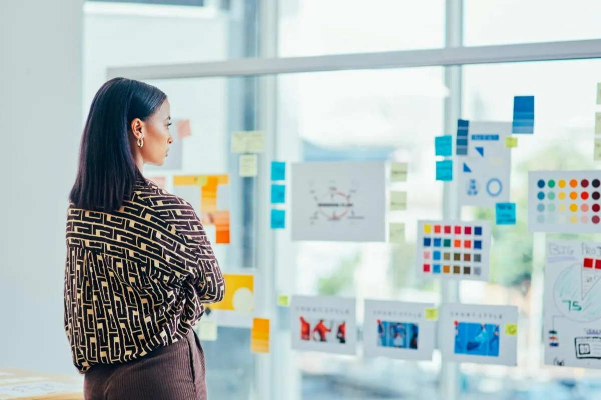 Rearview shot of a young designer brainstorming with notes on a glass wall in an office Woman in front of post its on a glass wall