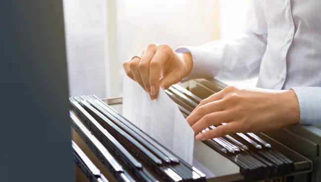 Hands searching through hanging files in a filing cabinet