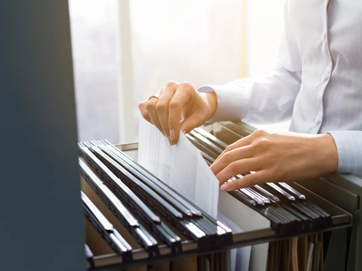 Hands searching through hanging files in a filing cabinet